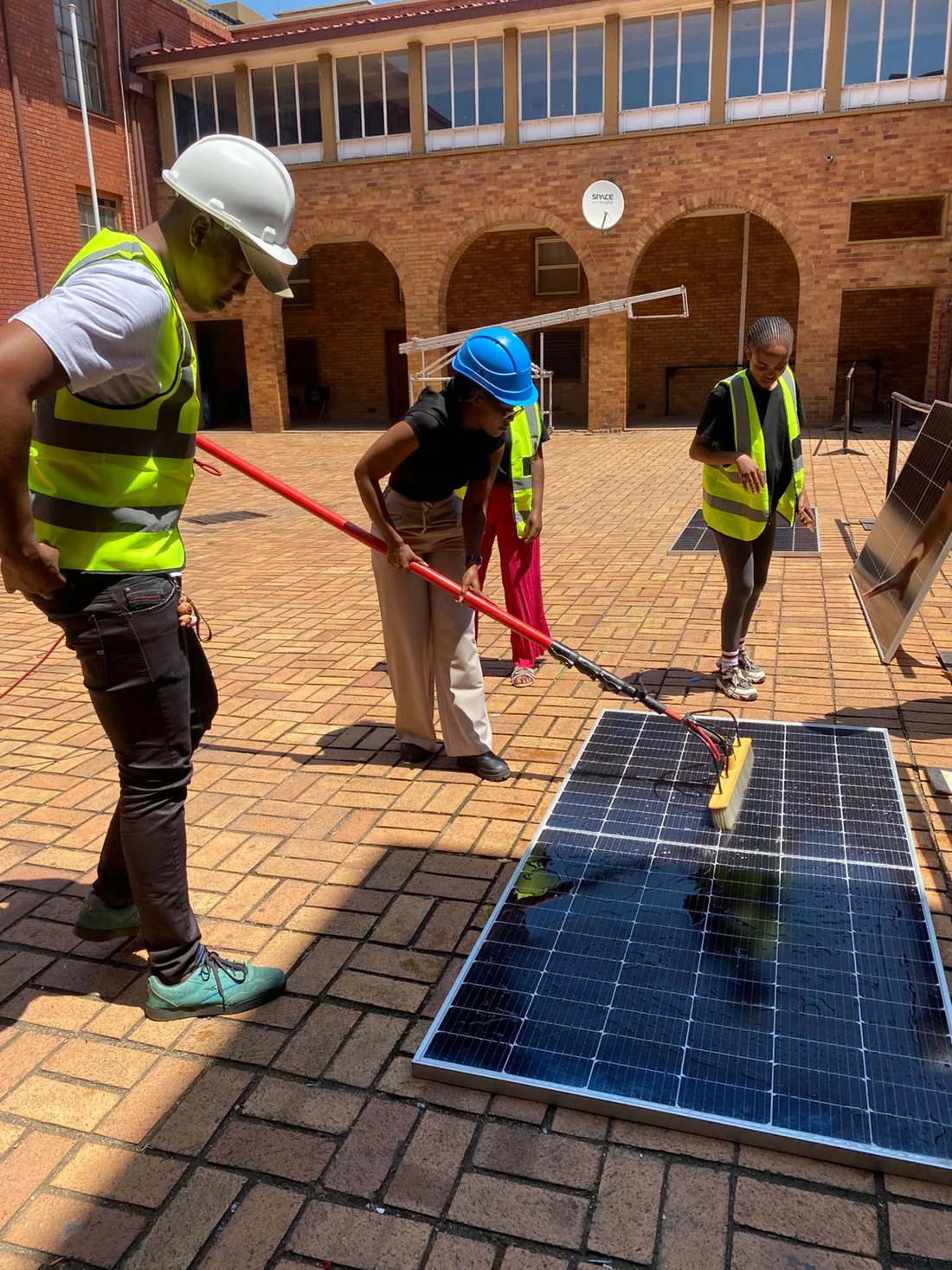 Learners using long-handled brushes to clean solar panels